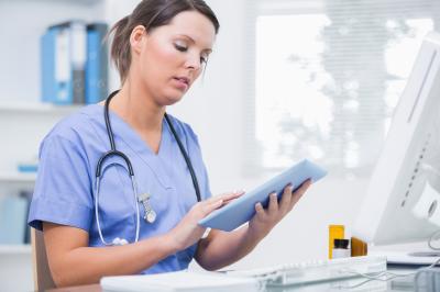Sitting nurse using tablet at desk.